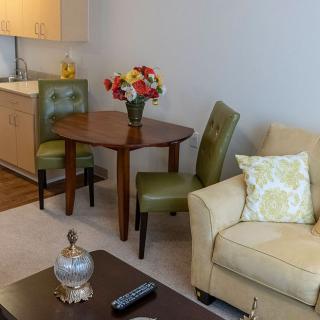 A cozy living room with a sofa, a wooden table, green chairs, and a vase of colorful flowers.