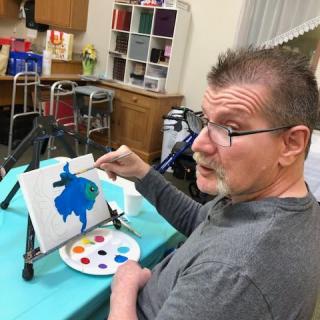 A man engaged in painting on a canvas indoors, with art supplies around him.
