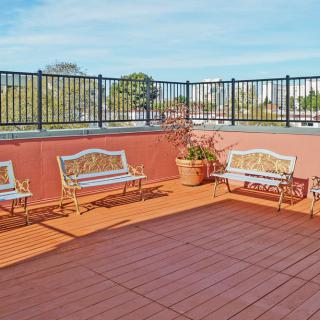 A spacious outdoor patio with wooden benches and potted plants, enclosed by a tall fence.