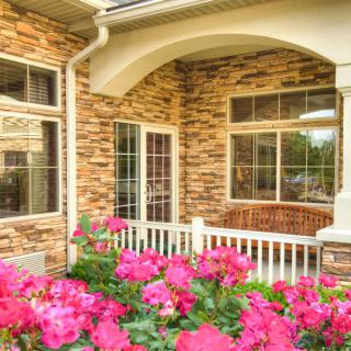 A charming house with a stone exterior and a porch, surrounded by vibrant pink flowers.