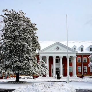 A picturesque view of a snow-covered building on campus, framed by a frosty tree.