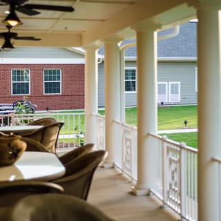 A cozy porch with columns and outdoor seating, overlooking a well-maintained lawn.