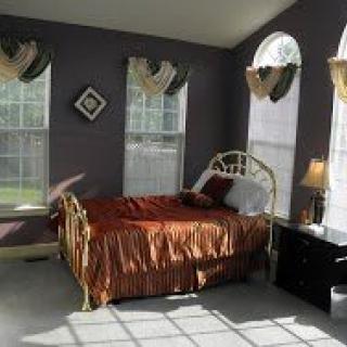 A cozy bedroom with a bed, windows, and a lamp illuminated by natural sunlight.
