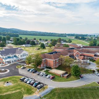 Aerial view of a building complex surrounded by lush greenery and distant mountains.