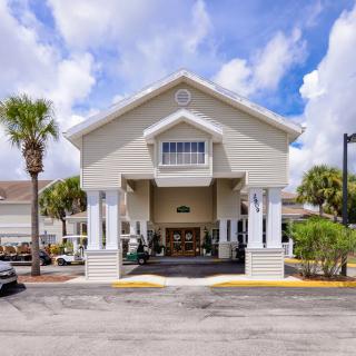 The exterior view of a hotel entrance with palm trees and a parking area under a partly cloudy sky.