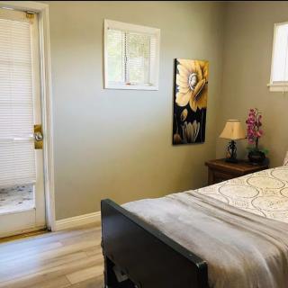 A cozy bedroom with a bed, nightstand, lamp, and wall art near a door and window.