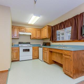 A cozy kitchen featuring wooden cabinets, a stove with an oven, and a window with curtains.