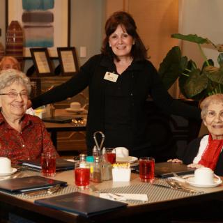 A group of seniors enjoying a meal at a restaurant, accompanied by a staff member.