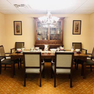 A well-furnished dining room with a chandelier, six chairs around a table, and a cabinet in the background.