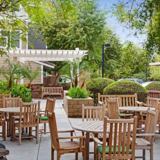 A peaceful outdoor patio with wooden tables and chairs surrounded by greenery.