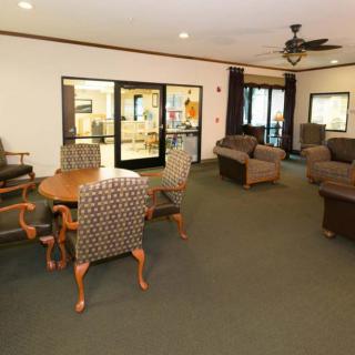 A cozy lounge area with upholstered chairs and a table, featuring a carpeted floor and a ceiling fan.