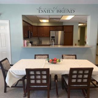 A dining area with a table set for six, connected to a kitchen.