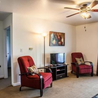 A cozy living room with red chairs, a television, artwork on the wall, and a ceiling fan.