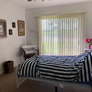 A cozy bedroom with striped bedding and wall art, featuring a large window with vertical blinds.