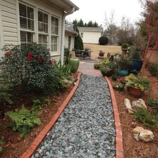 A landscaped garden pathway lined with plants and gravel leading to a patio area.