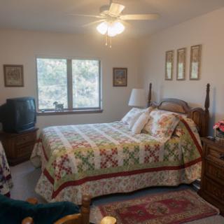 A cozy bedroom featuring a quilted bedspread, a television, and natural light coming through the windows.