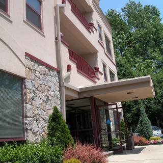 The exterior of a building with balconies and an entrance awning, surrounded by trees.