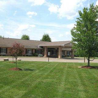 A building with a well-maintained lawn and surrounding trees under a partly cloudy sky.