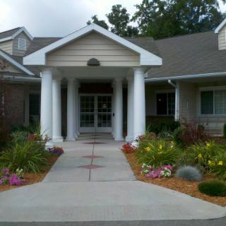 A welcoming house entrance with white columns and a landscaped garden.
