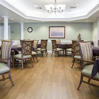 A well-arranged dining room with elegant chairs and tables, wooden flooring, and a chandelier.