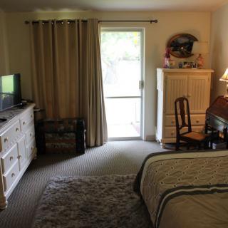 A cozy bedroom with a bed, television, dresser, and desk near a window.