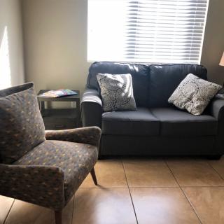 A cozy living room with a sofa, armchair, and natural light from a window.