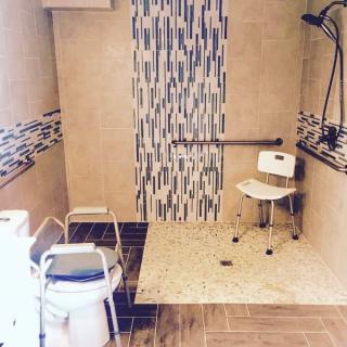 A modern accessible bathroom featuring a shower with grab bars and a chair.