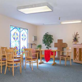 A serene chapel interior featuring wooden furniture, a cross, and stained glass windows.