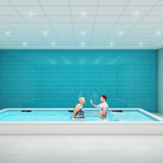 Two people engaging in aquatic therapy in an indoor pool with blue tiled walls.