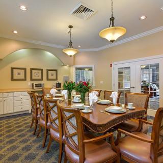 A well-lit dining room with a long table set for a meal, surrounded by wooden chairs and warm decor.