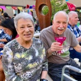 An elderly couple smiling at a social gathering outdoors.