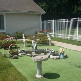 A serene garden with a birdbath, decorative elements, and a fenced yard on a sunny day.
