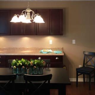 A cozy dining area with a table set with flowers, under warm lighting, adjacent to the kitchen cabinets.