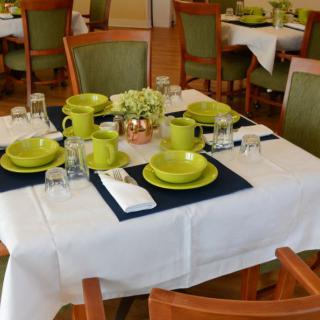 A restaurant dining table set with green dishware and neatly arranged place settings.