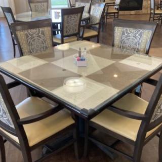 A dining area with a square glass-top table surrounded by four chairs.
