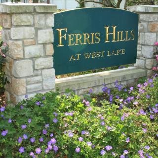 A stone sign for 'Ferris Hills at West Lake' surrounded by blooming flowers.