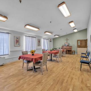 A dining area with neatly arranged tables and chairs, large windows, and bright lighting.