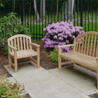 A serene garden patio with a wooden bench and chair, surrounded by blooming flowers.