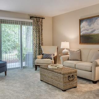 A cozy living room featuring a sofa, armchair, and coffee table with a lamp and artwork on the wall.
