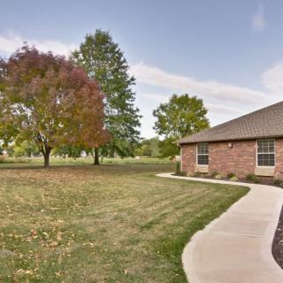 A suburban brick house with a neatly maintained lawn and trees in the background.