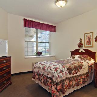 A traditional bedroom with a single bed, floral bedding, and a dresser under a curtained window.