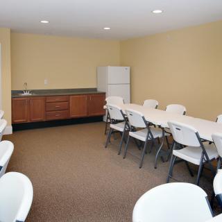 A small conference room with folding chairs and tables, featuring beige walls and a carpeted floor.