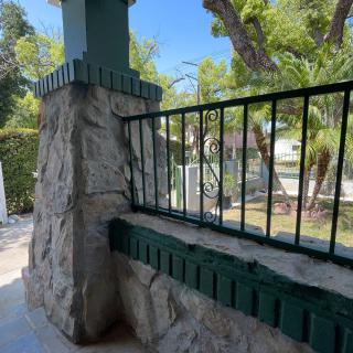 A stone pillar with an iron railing overlooks a sunny garden area.