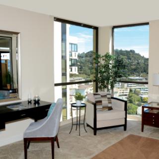 A modern office space with large windows offering a city view, featuring a desk, chair, and an indoor plant.