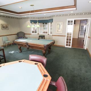 A cozy game room with a pool table and card table, featuring carpet flooring and elegant lighting.