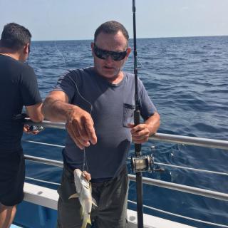 A man holding a fishing rod on a boat in the ocean, having just caught a fish.