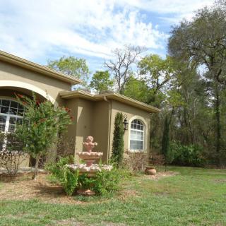 A stucco house with a garden and fountain in the yard, surrounded by trees.