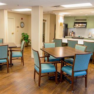 A cozy dining area with teal upholstered chairs and wooden tables, adjacent to an open kitchen space.