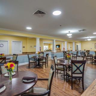 A spacious dining room with neatly arranged tables and chairs, featuring warm lighting and floral decorations.
