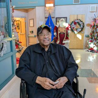 An elderly man sitting comfortably in a wheelchair, surrounded by festive holiday decorations.